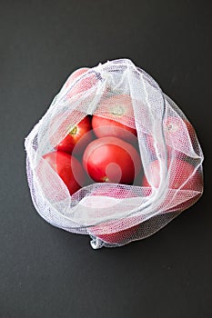 Reusable eco-friendly bag full of fresh seasonal tomatoes on black background