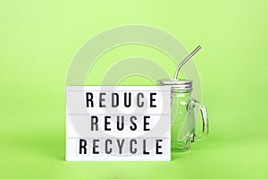 Reusable glass jar with metal straw and cinema lightbox on the light green drop