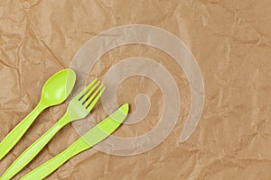 Reusable recyclable green fork, spoon, knife made from corn starch on brown crumpled craft paper, copy space. Eco, zero waste,