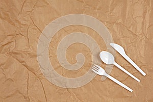 Reusable recyclable white fork, spoon, knife made from corn starch on brown crumpled craft paper, copy space. Eco, zero waste,