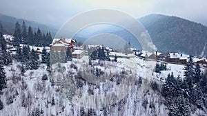 Revealing aerial of inhabited locality in the mountains on winter. Mountain village buildings on snowy hill slopes