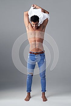 Revealing the body of a greek god. Studio shot of a handsome young man undressing against a grey background.