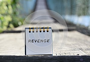Revenge text written on white note with blurred background of hanging bridge