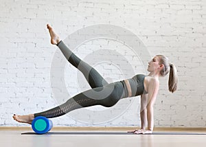 Reverse plank exercise with foam roller. Young fit woman does pilates in loft fitness studio, indoor.