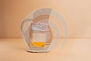 reverse side view of creative cardboard crafting: plastic bag with yellow liquid glued to a brown paper pitcher