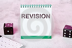 REVISION text on a white notepad sheet next to dice on an abstract background