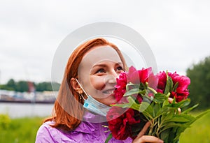 Revival after coronavirus. Smiling happy redhead woman sniffs pink flowers