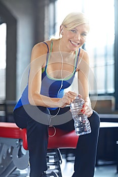 Reviving after a workout. Portrait of a beautiful young woman listening to music and taking a water break at the gym.