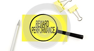 REWARD PERFORMANCE text on the sticker through magnifier. View from above. Business concept