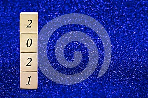 Wooden cubes with numbers 2021 on blue sparkling background.