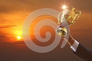 Reword of work . business hand in suit holding golden trophy with sun rise abstract multi color background ,  business concept