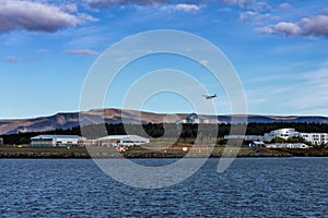 Landscape of Reykjavik, Iceland. Domestic airport and Perlan building. A small airplane in the air, bay of water in foreground.