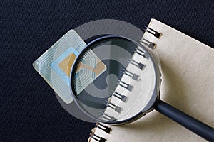 RFID tag transponder under magnifying glass, next to notepad. Concept for the use of wireless RFID technology in commerce,