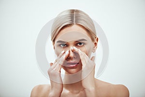 Rhinoplasty - nose surgery. Portrait of attractive blonde woman touching her nose and looking at camera while standing