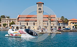 Excursion boat is driving along old Venetian watch tower at old seaport of Rhodes island, Greece