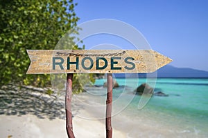 Rhodes wooden arrow road sign against beach with white sand and turquoise water background
