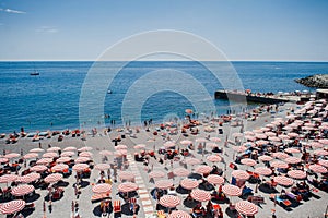 Rhythm of red umbrellas and tourists on a sunny beach in Genoa, Italy.