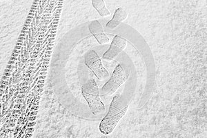 Rhythmic footprints, boot tracks and car tires on thin white snow in winter go into the distance, horizontal frame, ribbed tread