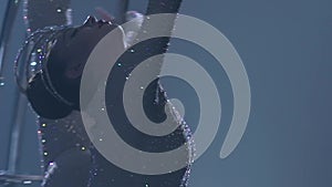 Rhythmic gymnastics the slips on one arm in the air on a metal moon rotating structure . Blue smoke background. Slow