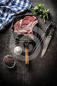 Rib eye steak in grill pan with herbs salt pepper fork and knife