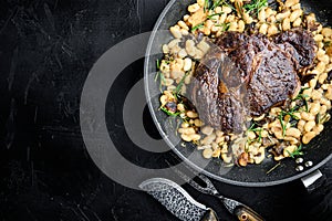 Rib eye steak with herbs, roasted beans, thyme and garlic, on frying cast iron pan, on black stone background, top view flat lay,