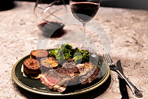 Rib eye steak with potatoes and broccoli and a glass of red wine, dining out, dinner, beef, medium rare.