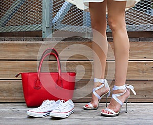 Ribbon Tie Stilleto shoe, sneakers and fashionable big red handbag. Fashionable woman with long beautiful legs standing