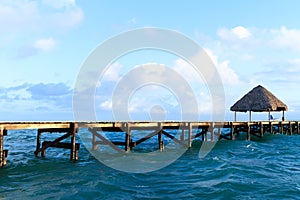 Ribbon wooden gazebo and chair on the beach at sunset or sunrise. Background of a seashore with seat, resting pavilion, palm trees