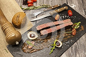 Ribeye steak from marble beef meat with vegetables and barbecue sauce. Served on a plate of black stone with fork and knife .