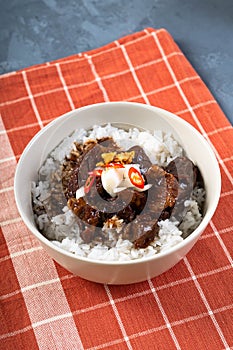 A rice bowl of chinese braised beef shank topped with red onion and chili pepper