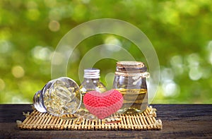 Rice bran oil capsule with red heart on wooden tabletop in greenery background