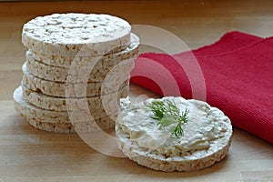 Rice cakes, one with cream cheese and herbs on wood, red napkin