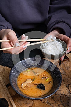 Rice on chopsticks on the background of tom yum soup. Eating Tom Yam.