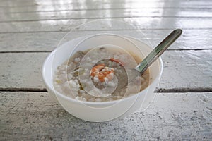 Rice congee mixed with shrimp and pork in white bowl and spoon.