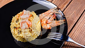 Rice dish of fried shrimp, mussels and octopuses on black plate on wooden background.