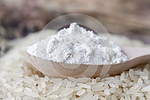 Rice flour in a spoon on a pile of white rice on old boards