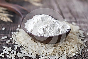 Rice flour in a spoon on a pile of white rice on old boards