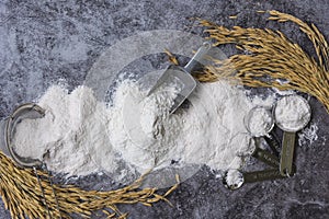 Rice flour Thai organic in a measuring spoon with wooden bowl on a pile of white rice, ear of paddy and strainer on concrete