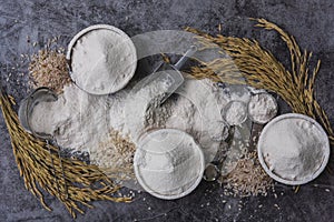 Rice flour Thai organic in a measuring spoon with wooden bowl on a pile of white rice, ear of paddy and strainer on concrete