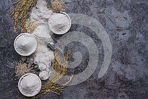 Rice flour Thai organic in a measuring spoon with wooden bowl on a pile of white rice, ear of paddy and strainer on concrete