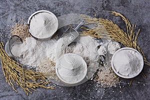 Rice flour Thai organic in a measuring spoon with wooden bowl on a pile of white rice, ear of paddy and strainer on concrete