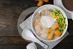 Rice gruel or Rice porridge with pork, onsen egg and deep fried dough stick in white bowl on wooden table