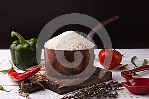 Rice in iron stewpan with vegetables on wooden cutting plank. Black background