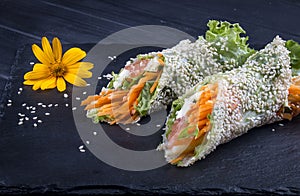 Rice paper rolls with sesame, vegetables and tuna. Asian dish. On a dark stone. Healthy food