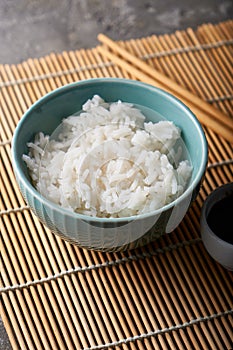 Rice in a porcelain bowl, with Japanese chopsticks, soy sauce, served on a gray stone table