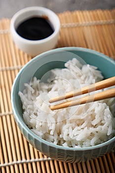 Rice in a porcelain bowl, with Japanese chopsticks, soy sauce, served on a gray stone table