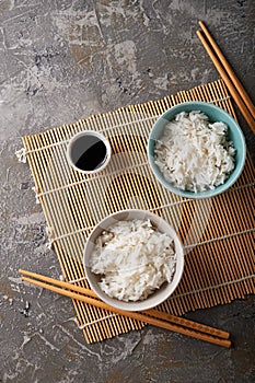 Rice in a porcelain bowl, with Japanese chopsticks, soy sauce, served on a gray stone table