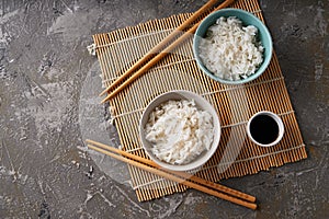 Rice in a porcelain bowl, with Japanese chopsticks, soy sauce, served on a gray stone table