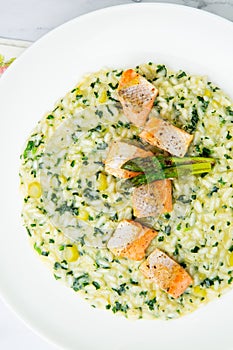 rice porridge with artichoke, red fish and herbs in a white plate, top view