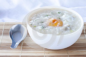 Rice porridge or congee with egg in white bowl and spoon on table.